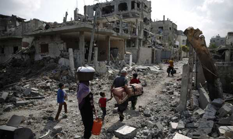 A Palestinian family carries their belongings towards the remains of their destroyed home 