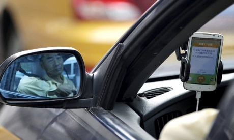 A taxi driver is reflected in a side mirror as he uses the Didi Chuxing car-hailing application in B