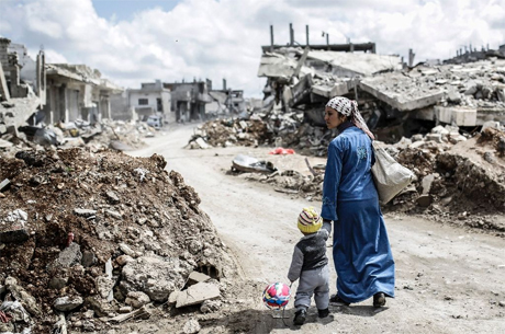 Kurdish Syrian woman walks with her child past the ruins of the town of Kobane