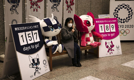 A woman removes her mask before taking pictures with the mascots of the Tokyo 2020 Olympics and Para