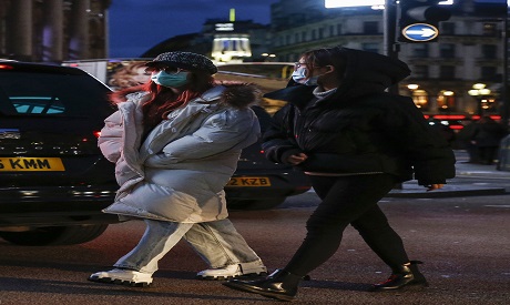 Two women cross street wearing masks in London