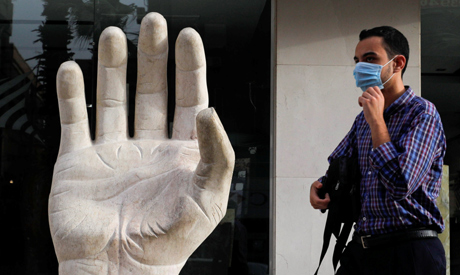 A man wearing a protective face mask walks near a granite symbol hand of peace, amid concerns over t