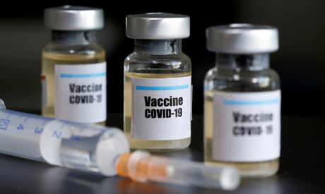 Small bottles labeled with a "Vaccine COVID-19" sticker and a medical syringe are seen in this illus