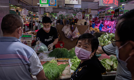 A vendor (2nd L) sells vegetables at his stall at a market in Beijing on June 20, 2020. (AFP)