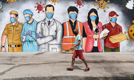 A man wearing a facemask walks past a mural on a garbage dump reading 