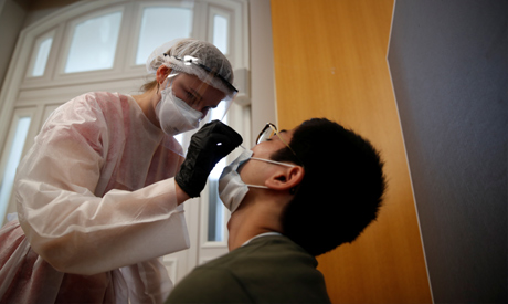 A health worker, wearing a protective suit and a face mask, administers a nasal swab to a patient at