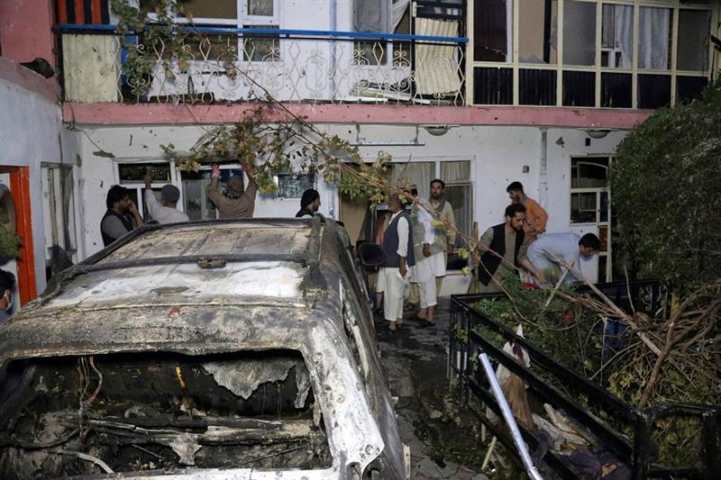 Afghan residents next to a damaged vehicle by US drone