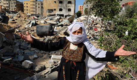 An elderly Palestinian woman reacts in front of her home, damaged by Israeli bombardment, in Beit La