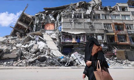 A Palestinian woman walks past a dsetroyed building in the al-Rimal commercial district in Gaza City