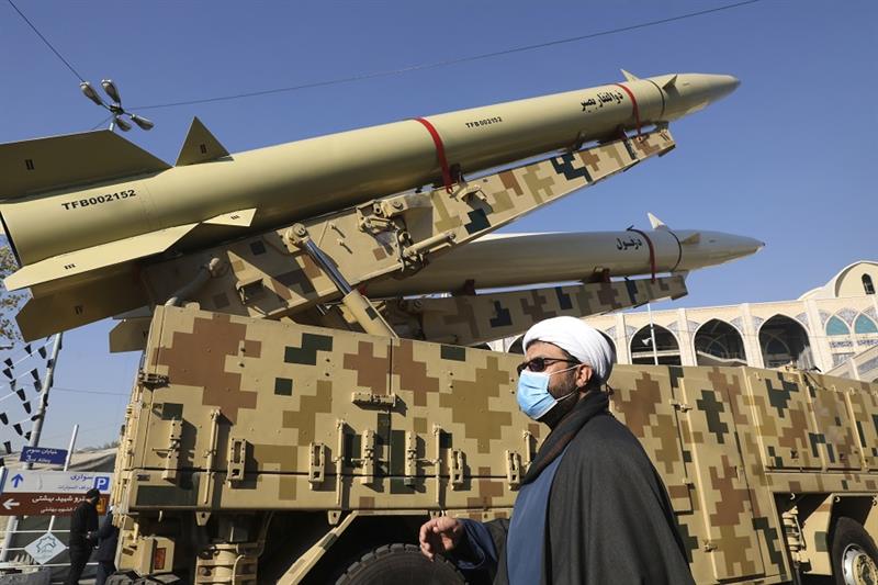 A cleric walks past Zolfaghar, top, and Dezful missiles