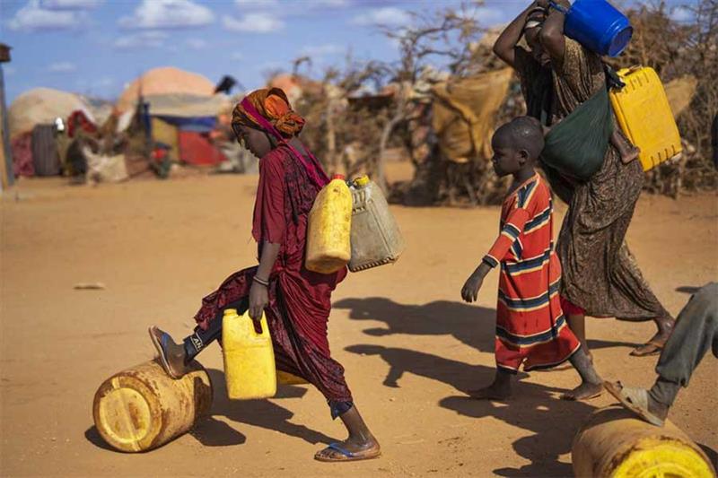 FILE - A Somali woman and children carry water at a camp for displaced people on the outskirts of Do