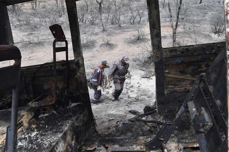 Algerian firefighters walk next to a charred bus in which at least 12 people were reportedly burnt t