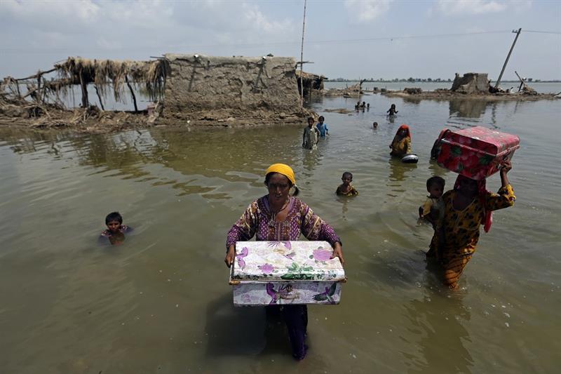 Women carry belongings salvaged from their flooded home after monsoon rains, in the Qambar Shahdadko