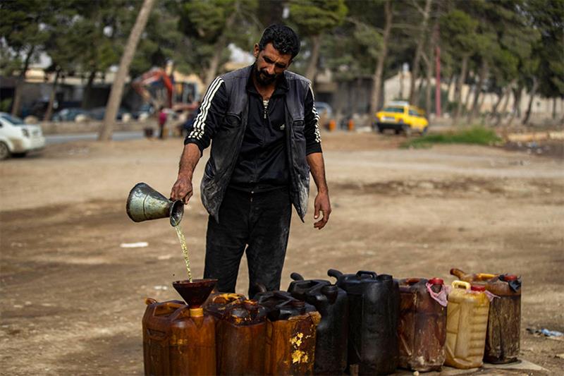 A Syrian man fills a container as he sells diesel on a roadside in the opposition held Syrian city o
