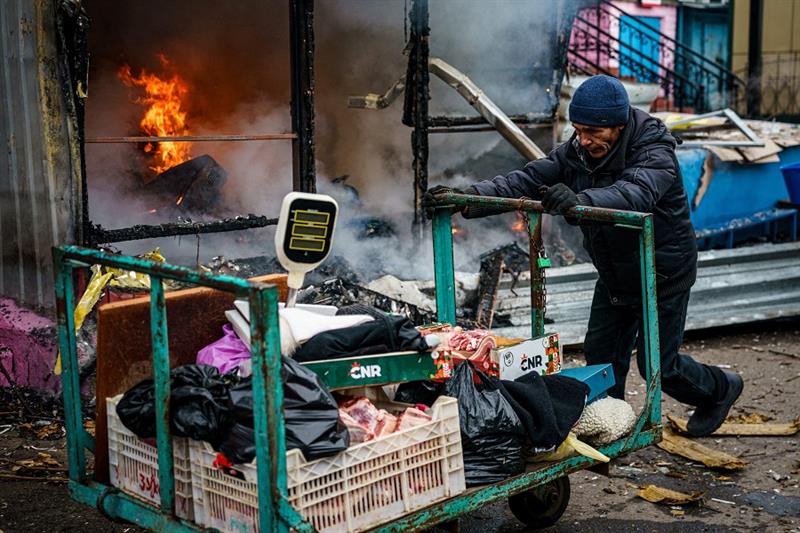 A man pushes a cart in front of a burning shop after shelling to city of Kherson, where five were ki