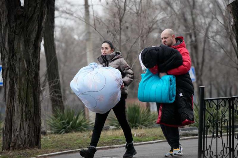 A couple carry their goods to a shelter during Russian shelling outside Mariupol, Ukraine, Thursday,