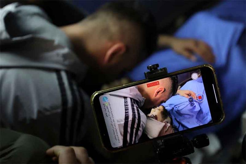 A man films with his mobile telephone as Palestinian mourners gather arround the body of Ahmed Amer 