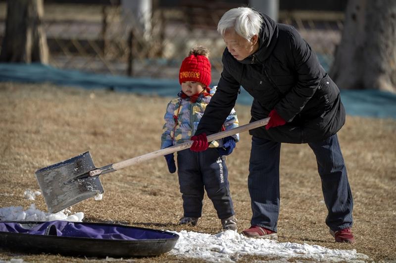 A child watches as an adult shovels snow at a public park in Beijing