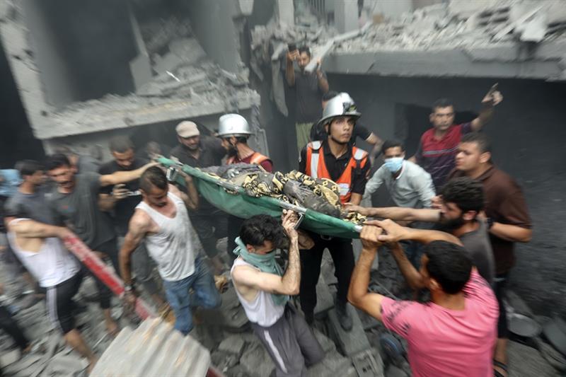 Palestinians carry a dead person who was found in the debris following Israeli airstrikes on Gaza Ci