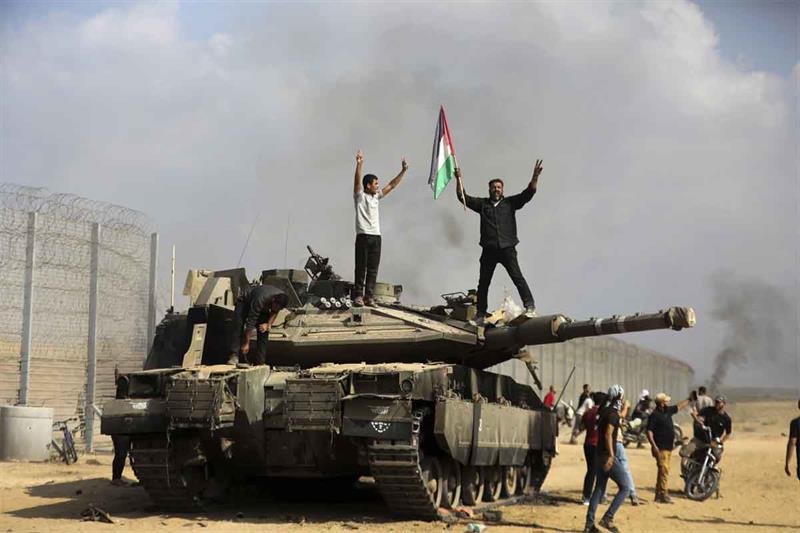 Palestinians wave their national flag and celebrate by a destroyed Israeli tank at the Gaza Strip fe