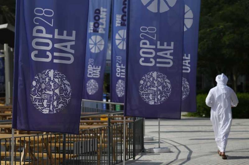 A person walks near signs for the COP28 U.N. Climate Summit, Tuesday, Nov. 28, 2023, in Dubai, Unite