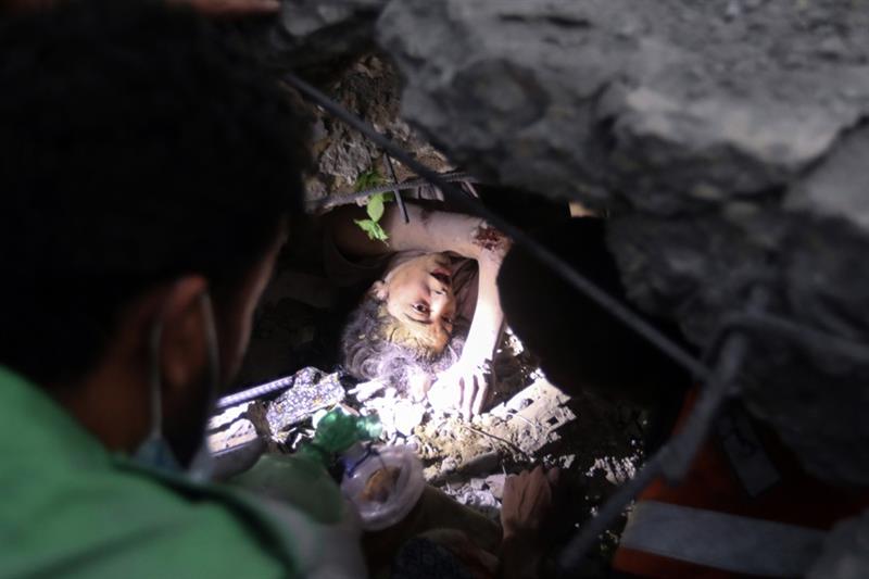 Palestinians try to rescue a girl stuck under the rubble of a destroyed building following Israeli a