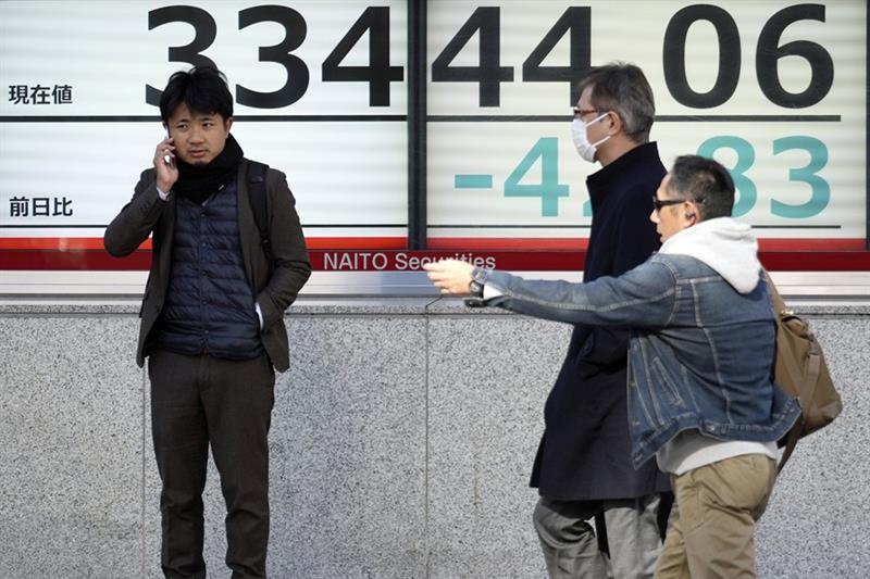 People walk in front of an electronic stock board showing Japan s Nikkei 225 index at a securities f