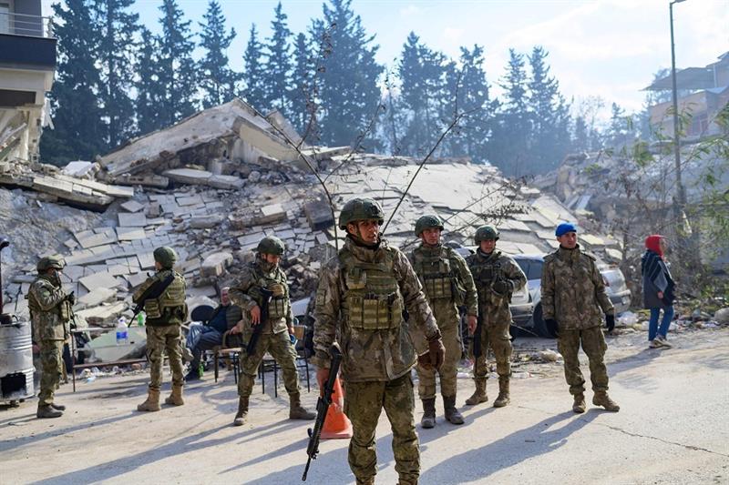 Turkish soldiers stand next to a destroyed building in Hatay 