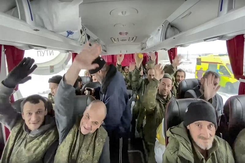 A group of Russian soldiers wave at a cameraman sitting in a bus after being released in a prisoners