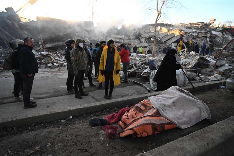 People stand next to victims  bodies near the rubble of collapsed buildings in Kahramanmaras, Turkey
