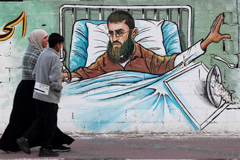 A Palestinian woman and her son walk past a mural depicting Khader Adnan, a Palestinian hunger strik
