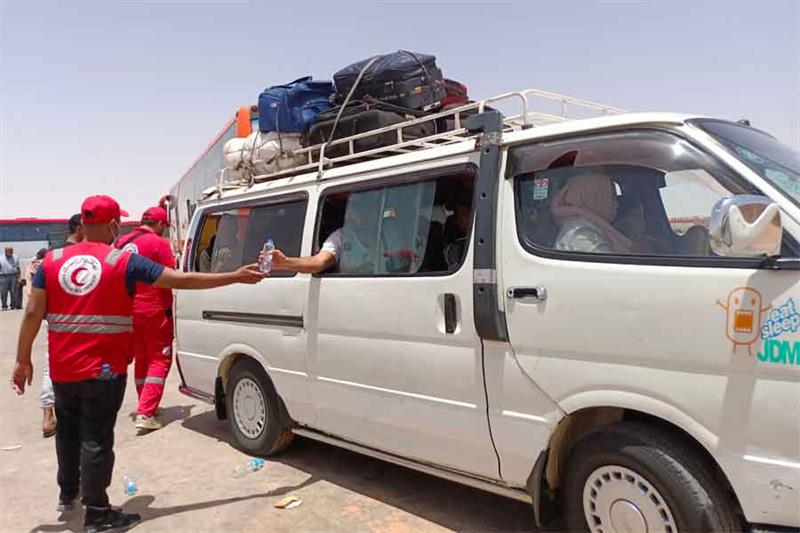  member of the Red Crescent passes a bottle of water to a refugee on a bus on the Egyptian side of t