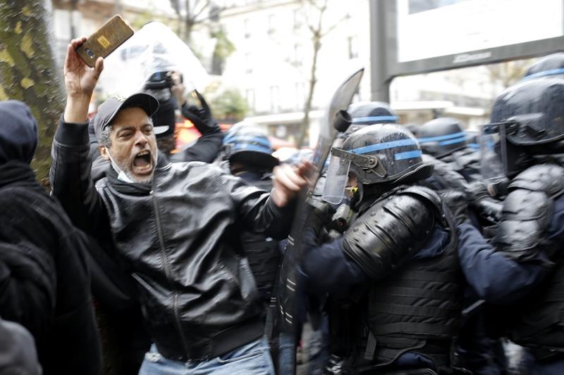 Riot police officers charge a man holding his phone during a protest rally in Paris, France, Saturda