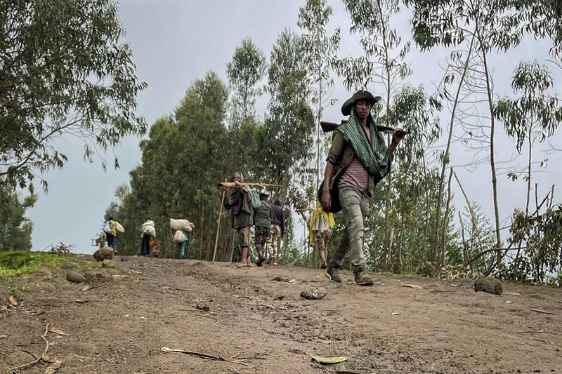 An unidentified armed militia fighter walks down a path as villagers flee with their belongings in t