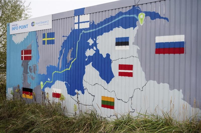 A sign reading  Nord Stream 2 Committed. Reliable. Safe.  hangs above a painted map of the Nord Stre