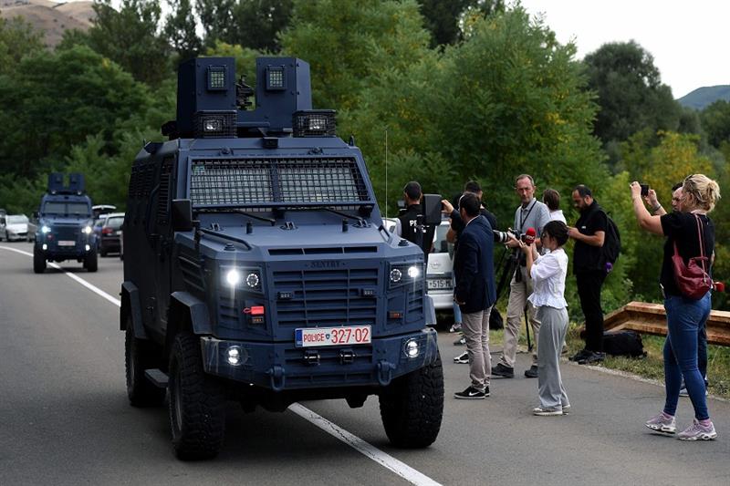 Kosovo s police vehicles drive past members of the public taking photographs near the entrance of th